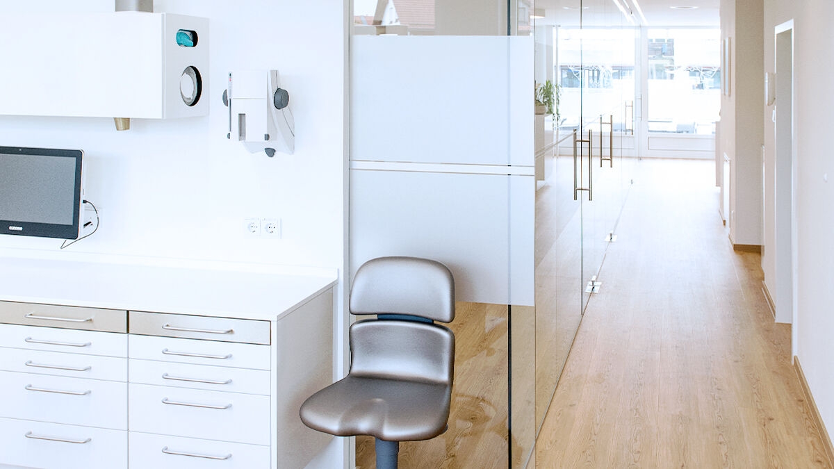 Hallway in a dentist's office, wooden floor and white furniture; in the foreground a swivel chair.